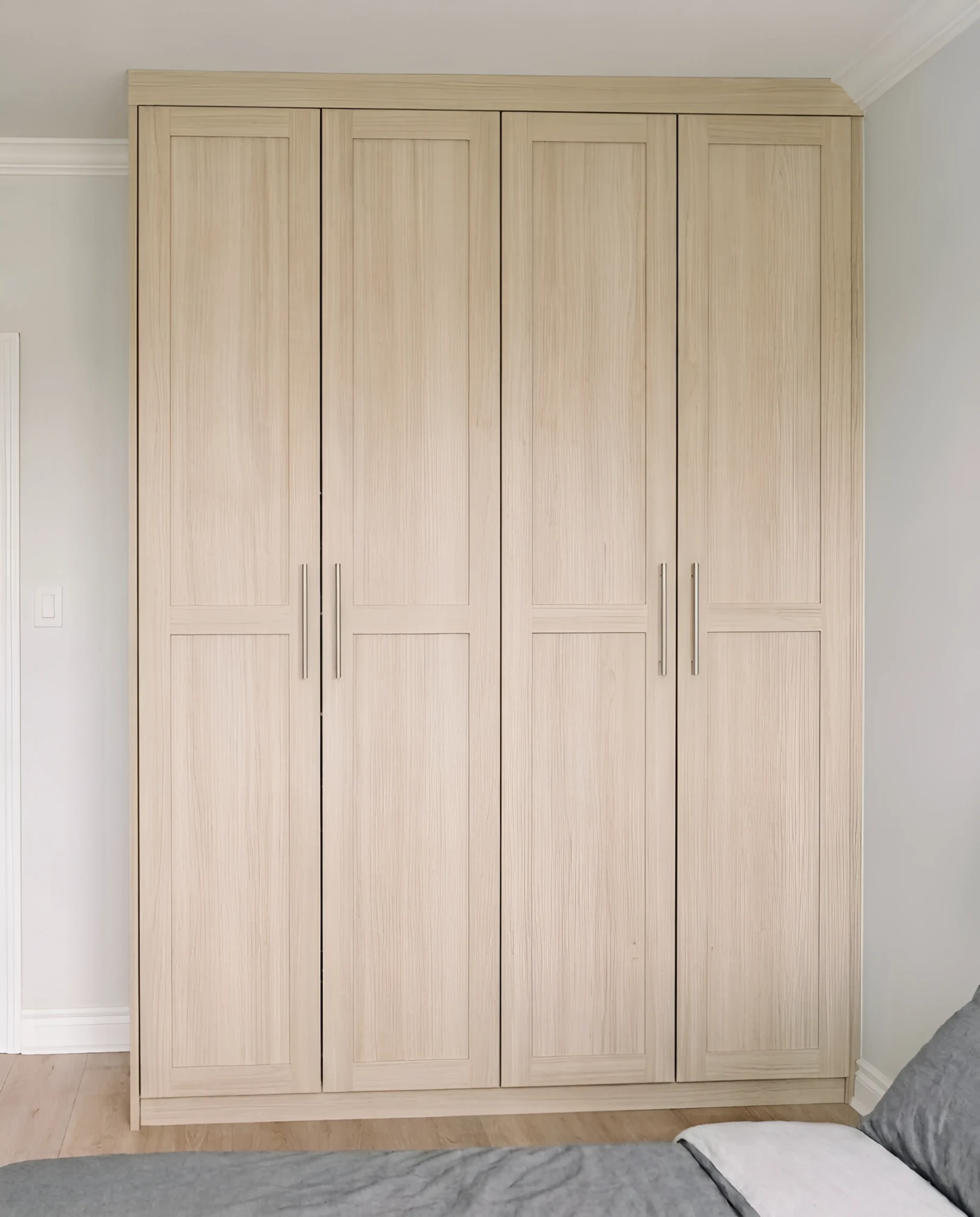 Light oak built-in wardrobe with four full-height shaker doors and long brushed handles, fitted floor to ceiling beside a bedroom door