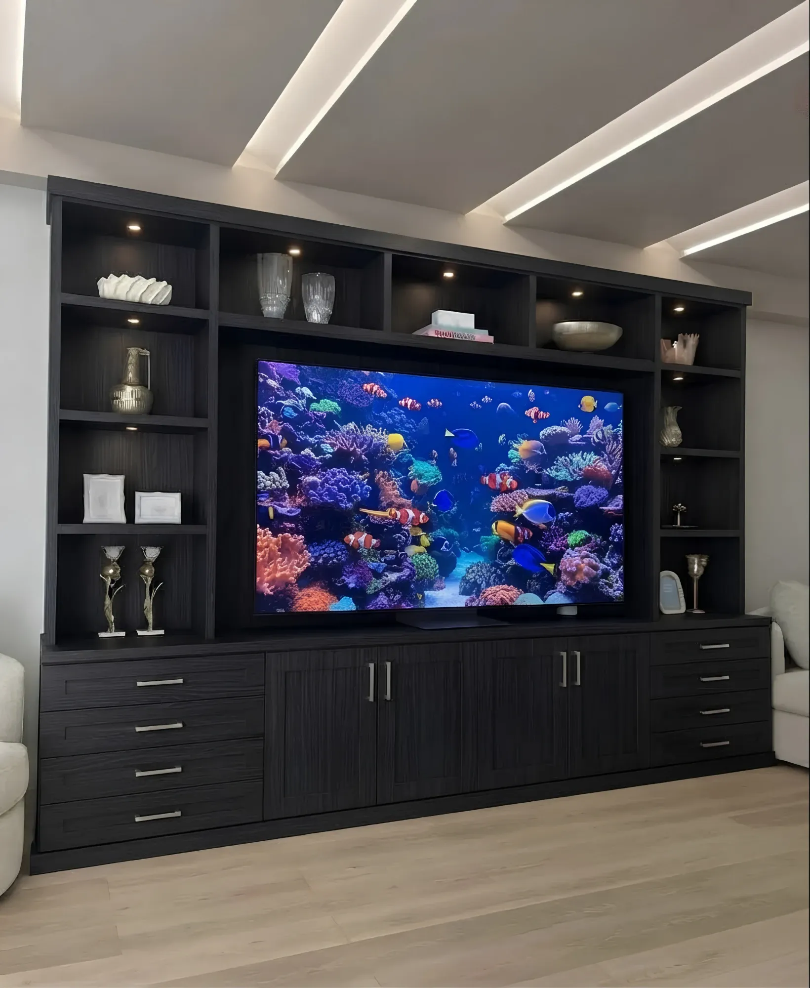 A black oak media wall with a large television set into lit display shelving over a run of cupboards and drawers