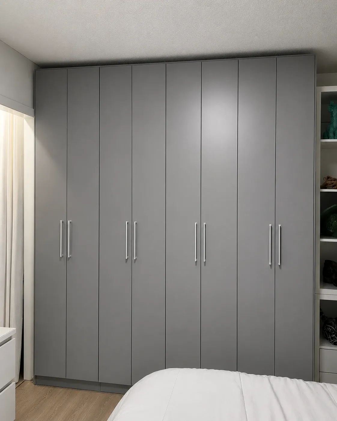 A grey wardrobe wall running floor to ceiling across a bedroom, eight full-height doors with white shelving returning down the side wall