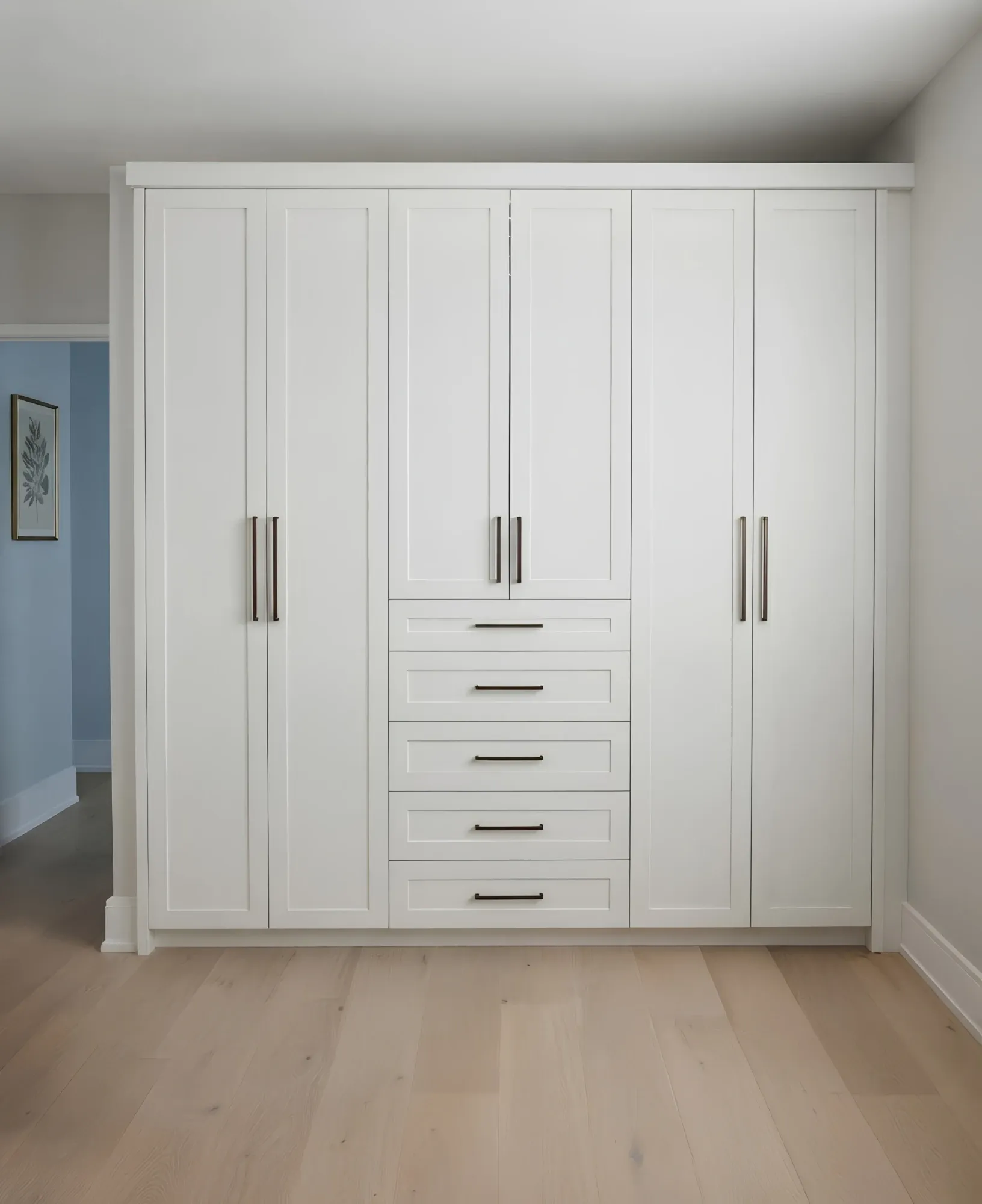 A white shaker wardrobe wall built floor to ceiling across a bedroom, six full-height doors with a stack of five drawers down the middle
