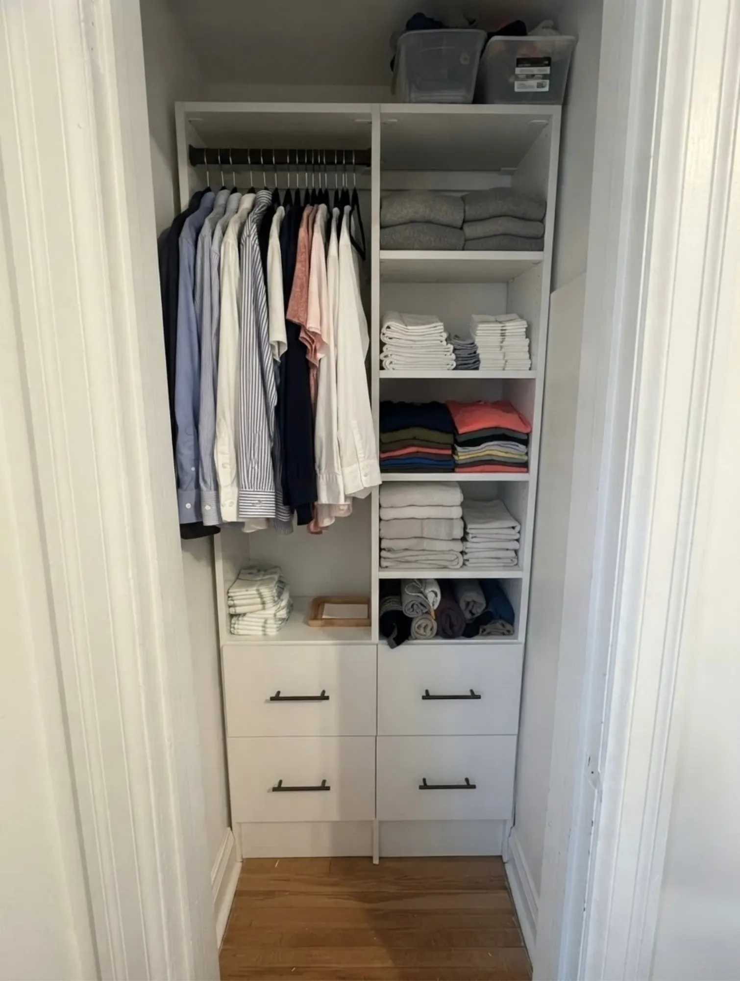 A white reach-in closet fitted into a narrow alcove, a single hanging rail beside a full-height tower of folded shelving over four drawers