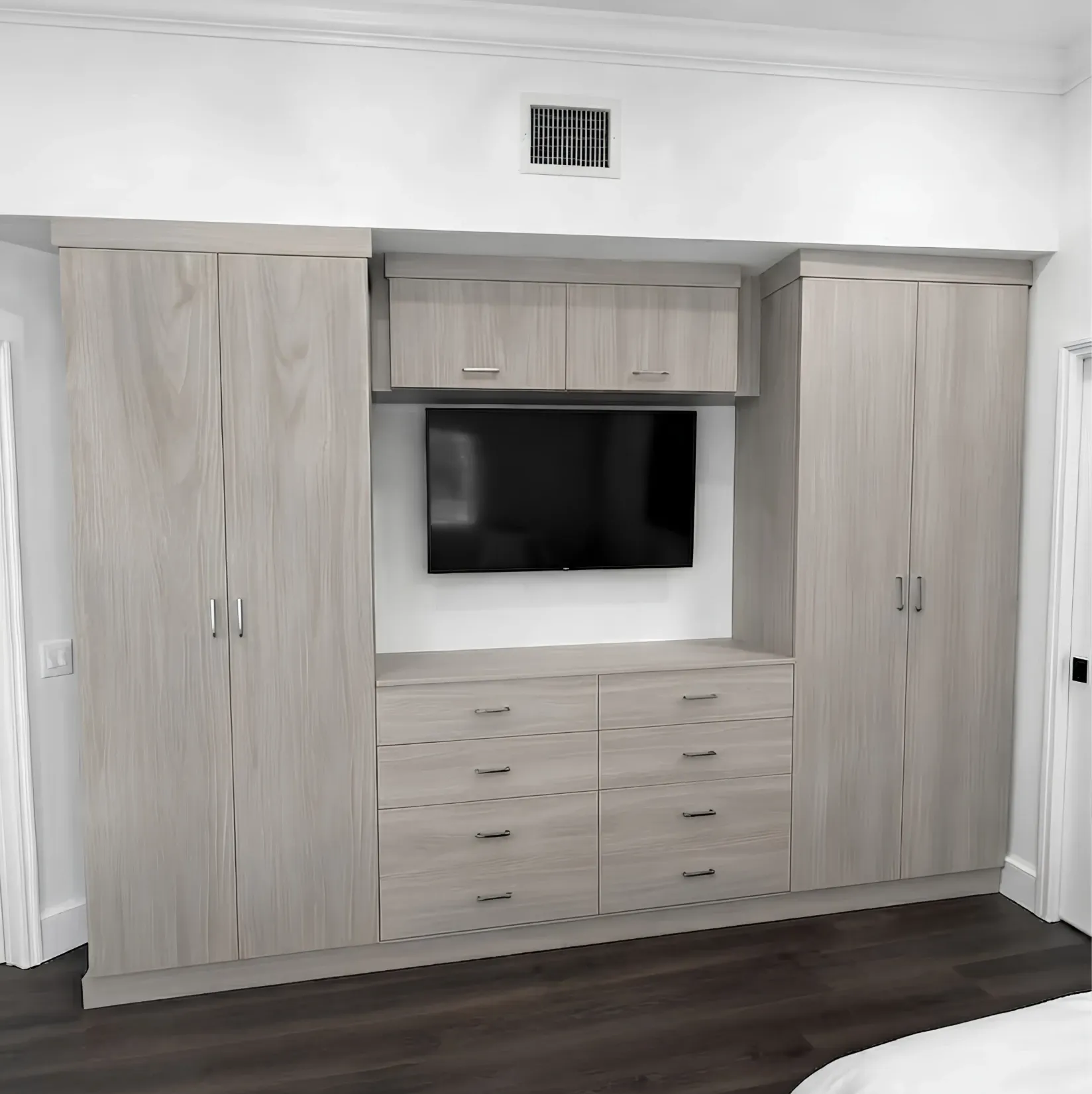 A pale oak wardrobe wall built into a Markham bedroom, a full-height cabinet at each end, six drawers under a wall-mounted television and a cupboard above it