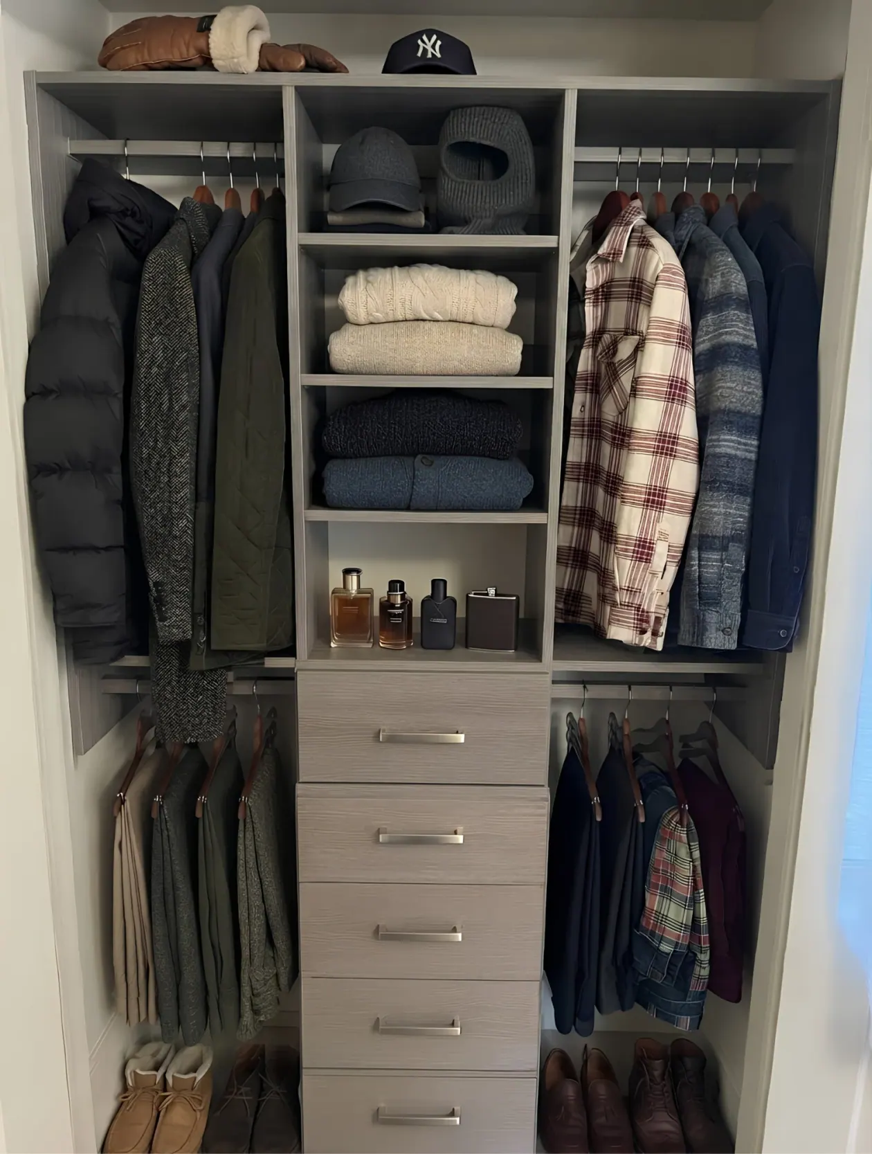 A grey oak reach-in closet with double hanging either side of a centre column of open shelves over five drawers