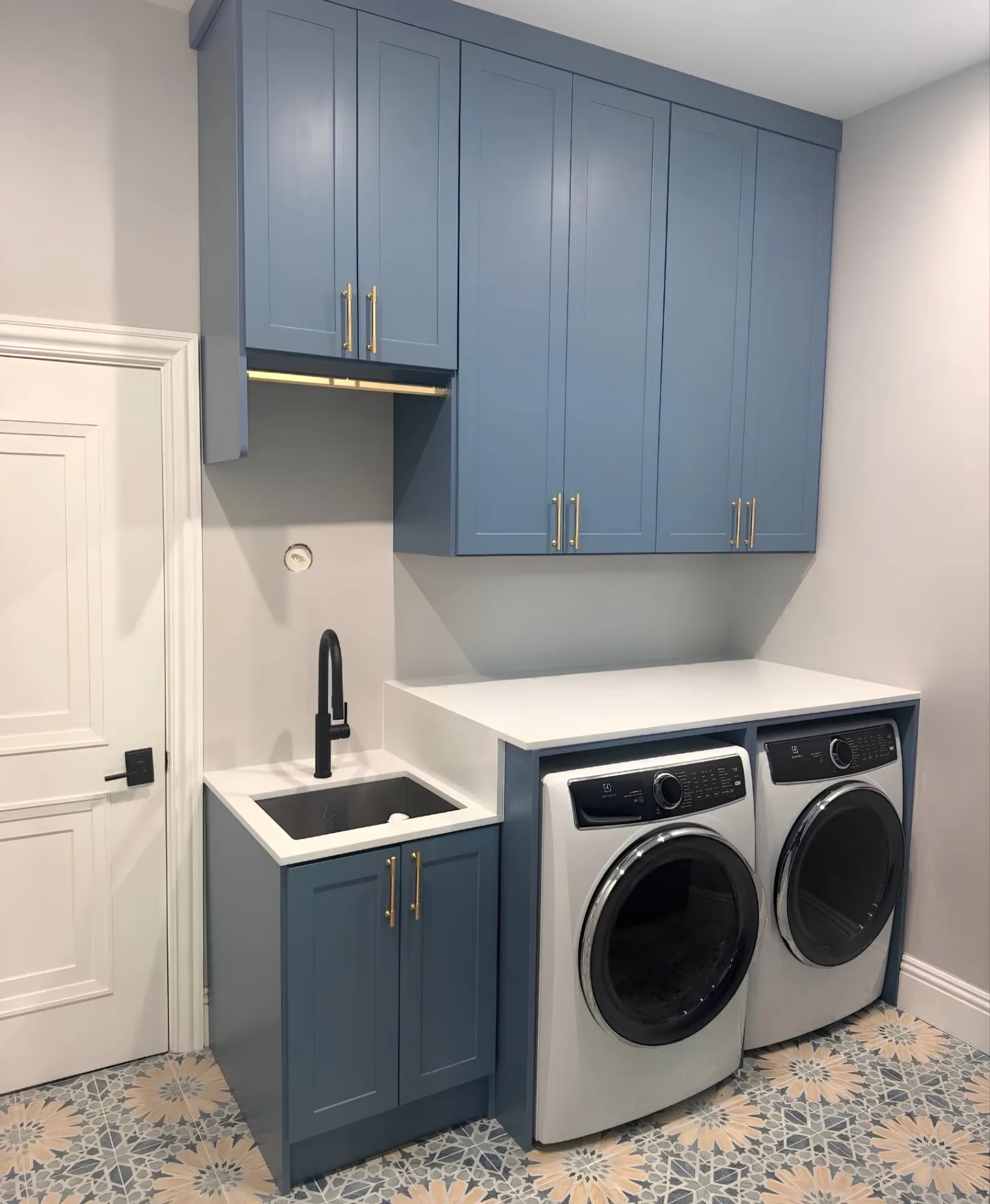Blue shaker wall cabinets with a hanging rail under a bridging unit, a quartz counter carried over a front-loading pair and a sink cabinet beside them on patterned tile
