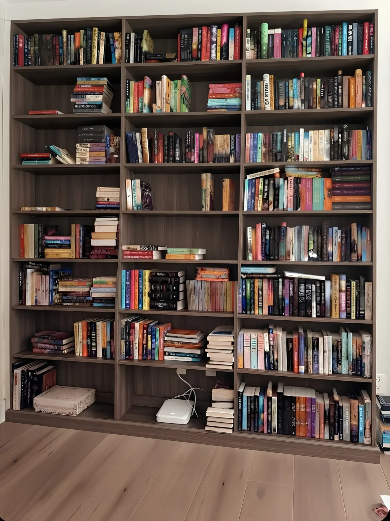A walnut library wall of three bays running floor to ceiling, every shelf full of books, against a pale wood floor