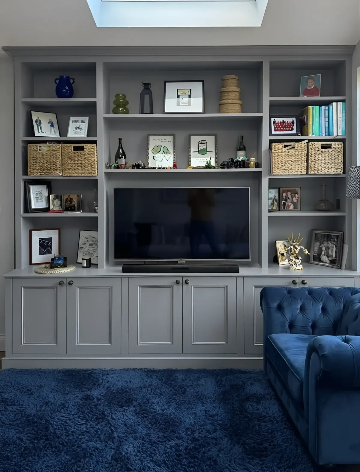 A grey painted media wall under a skylight - open display bays either side of a recessed screen and soundbar, over panelled cupboards