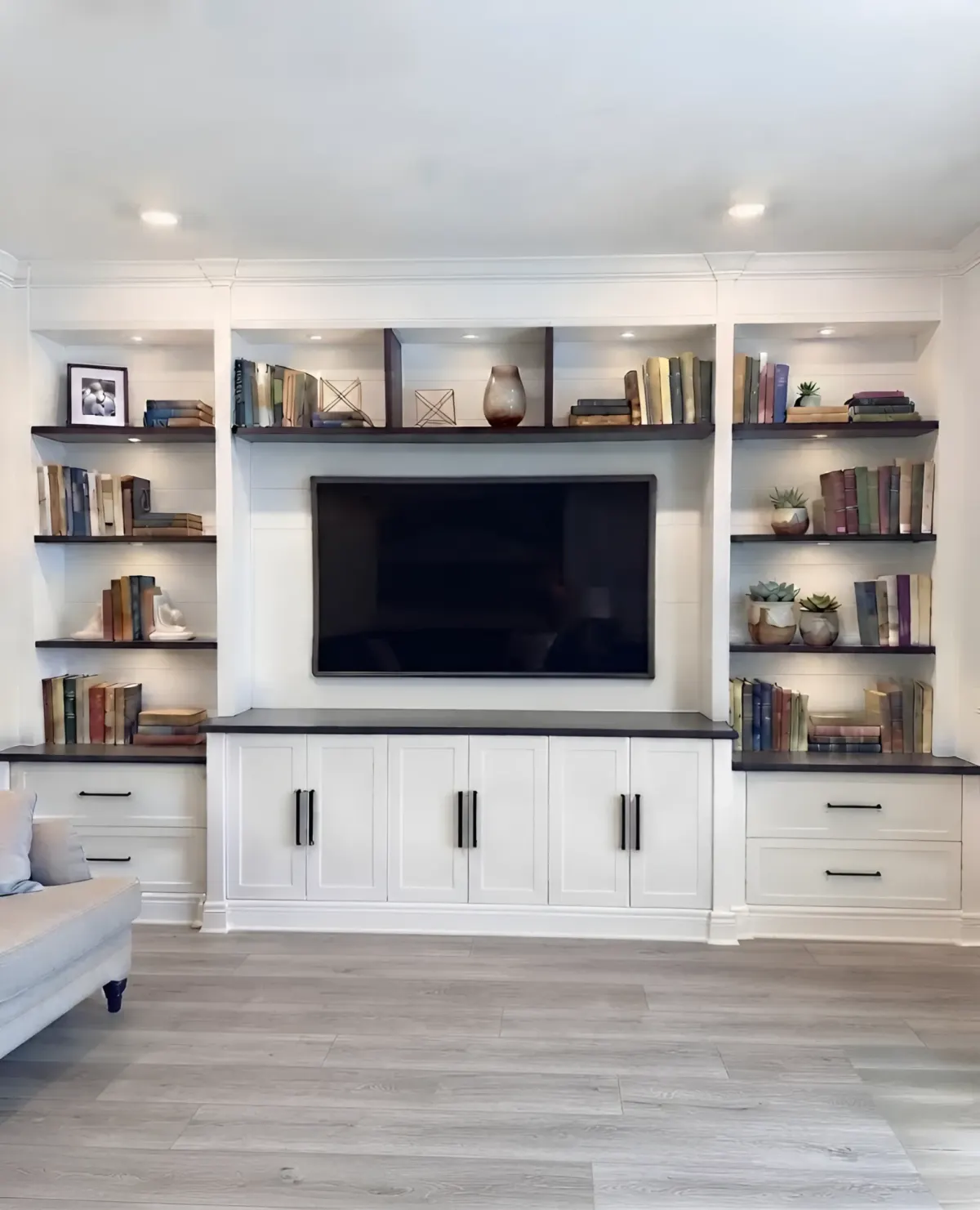 A white media wall with walnut floating shelves either side of the screen, a walnut counter across the base and closed cupboards under it