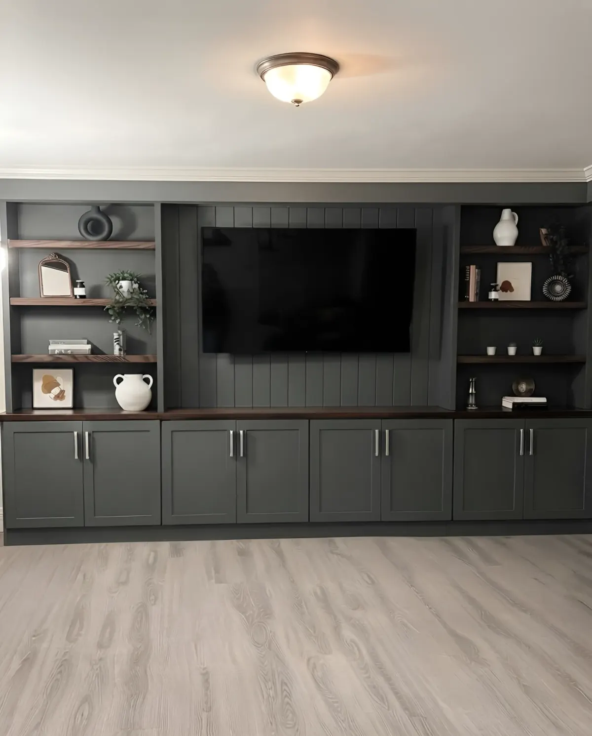 A charcoal media wall - the screen on a vertically panelled centre bay, walnut shelves either side and a walnut counter over a run of cupboards