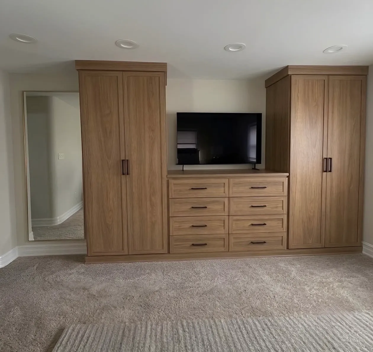 An oak media wall in a bedroom — a television over an eight-drawer dresser run, with full-height wardrobes either side