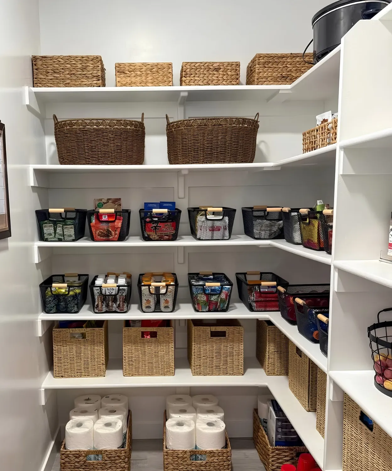 A white walk-in pantry shelved on two walls, lidded baskets along the top, mesh bins at eye level and woven baskets on the lowest shelf