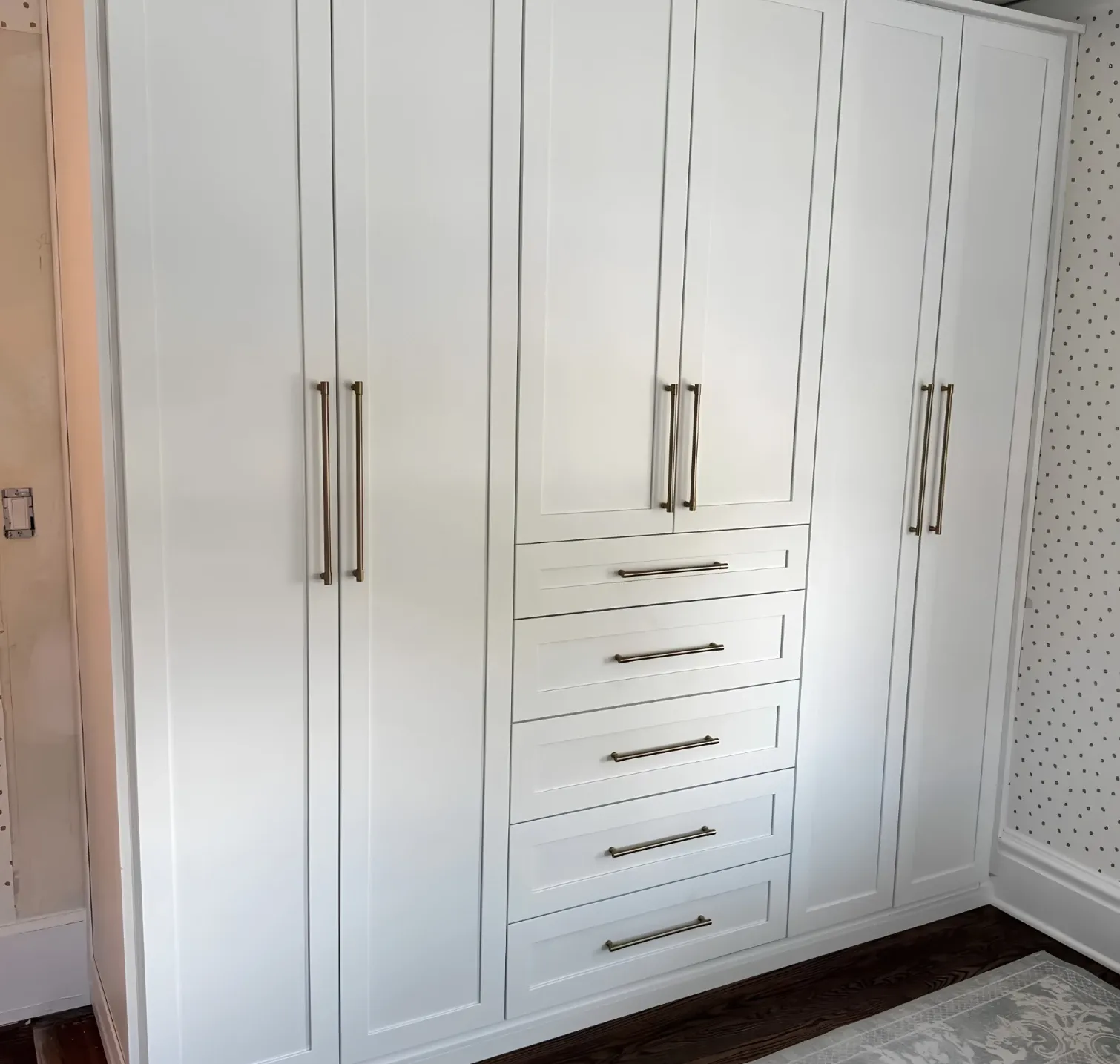 A white shaker wardrobe wall built the width of a Burlington bedroom, full-height doors either side of a bank of five drawers, finished to the floor on its own plinth