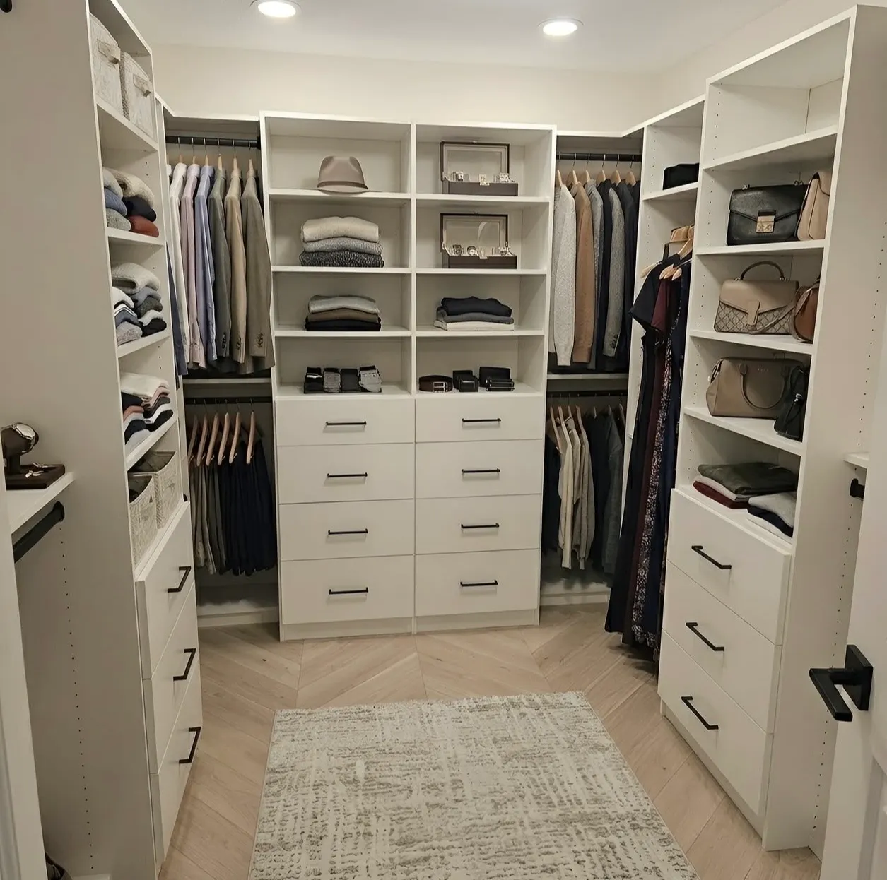 A white walk-in closet in a Mississauga home, hanging on both walls either side of a centre bank of eight drawers under open shelving