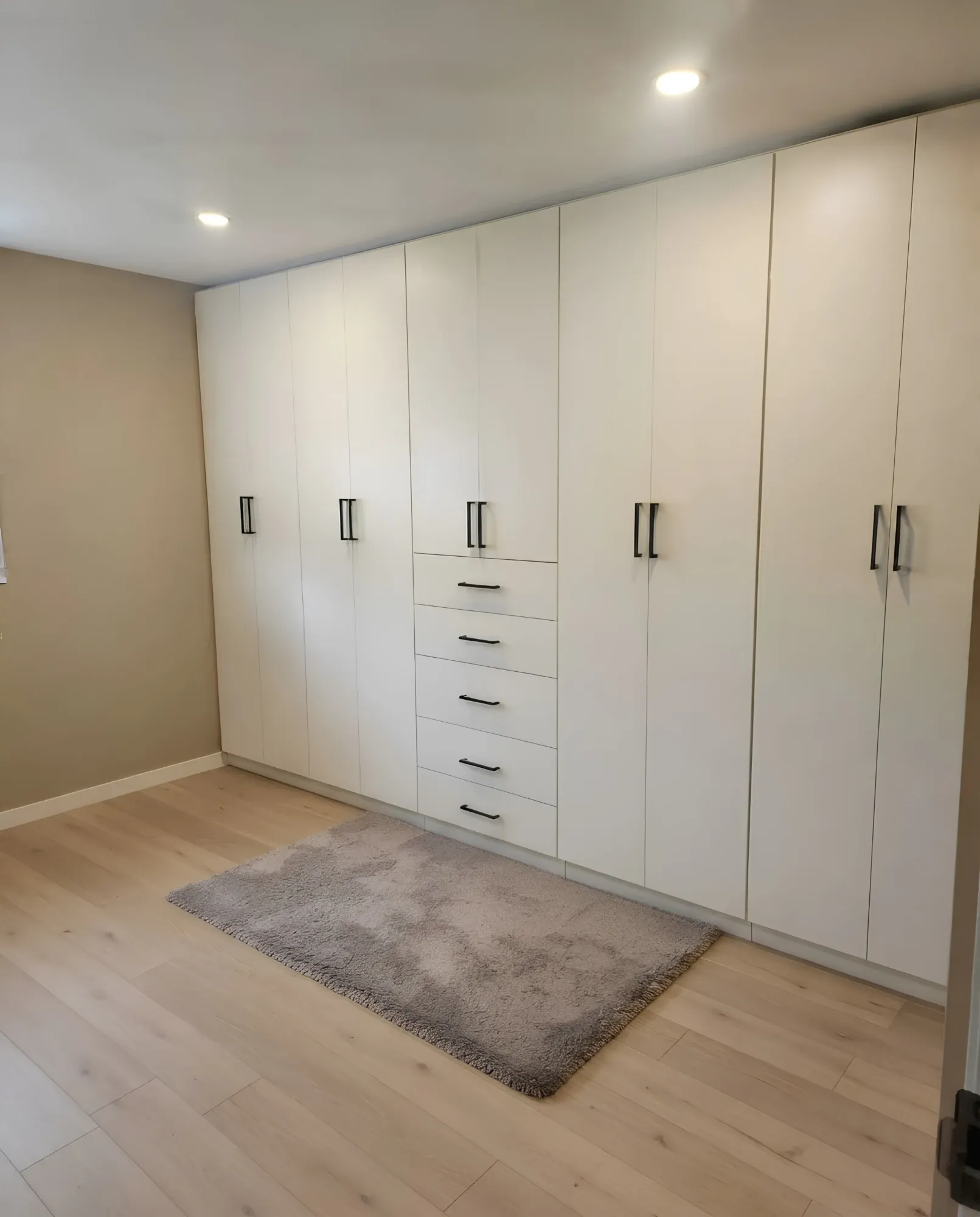 A white wardrobe wall running the length of an Oakville bedroom, full-height doors throughout with a stack of five drawers set into the middle bay