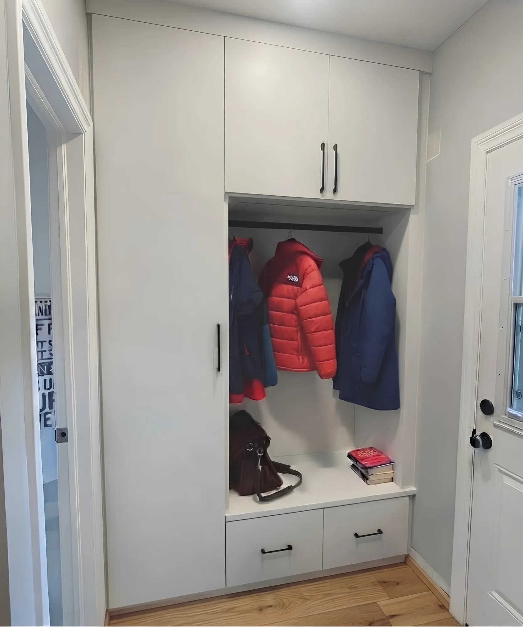 A white entry closet beside the back door, coats hung under a cupboard with a bench below and two drawers under the seat