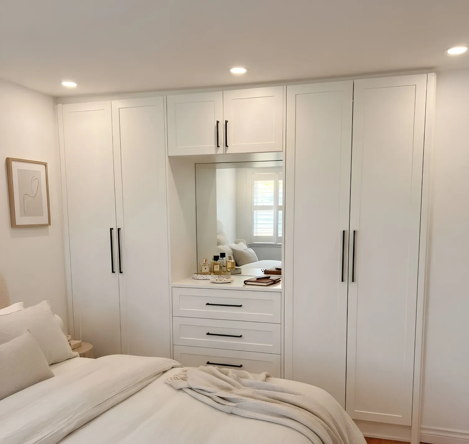 A white wardrobe wall built across an Oakville bedroom, full-height doors either side of a mirrored dressing recess over three drawers, finished to the room's own trim