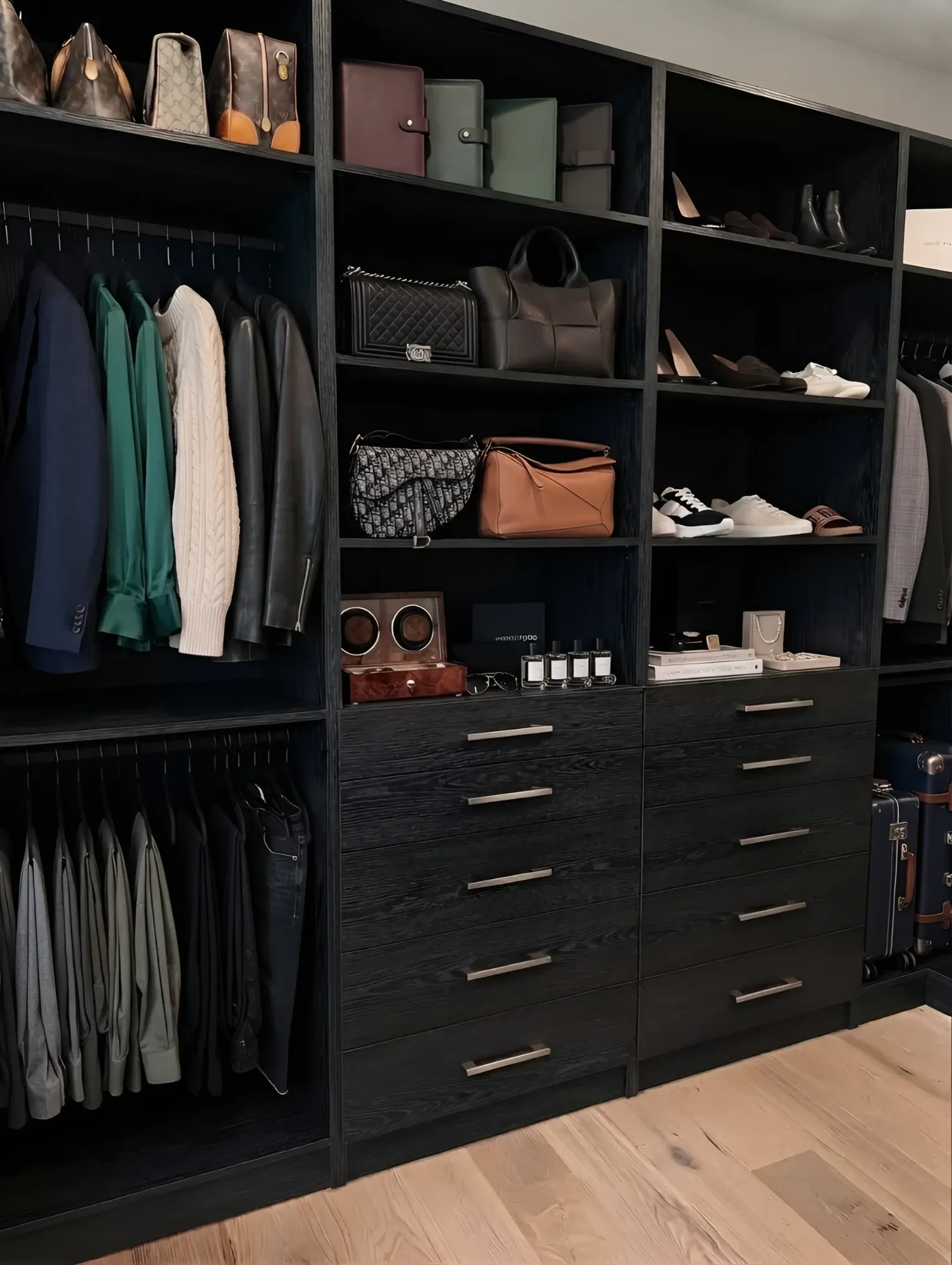 A black oak walk-in closet with hanging at two levels, open shelving for handbags and shoes, and two banks of five drawers under a display run