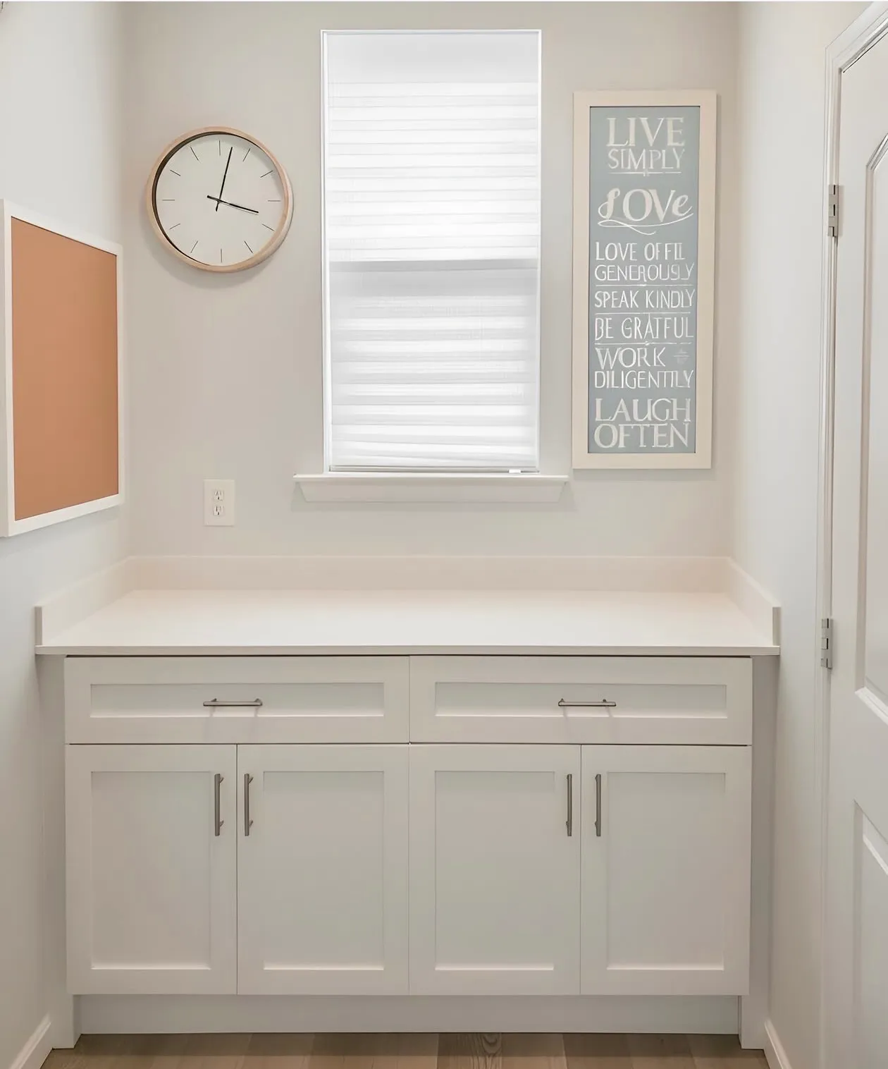 A white laundry run under a window, two drawers over four shaker cupboard doors with a full-width folding counter above
