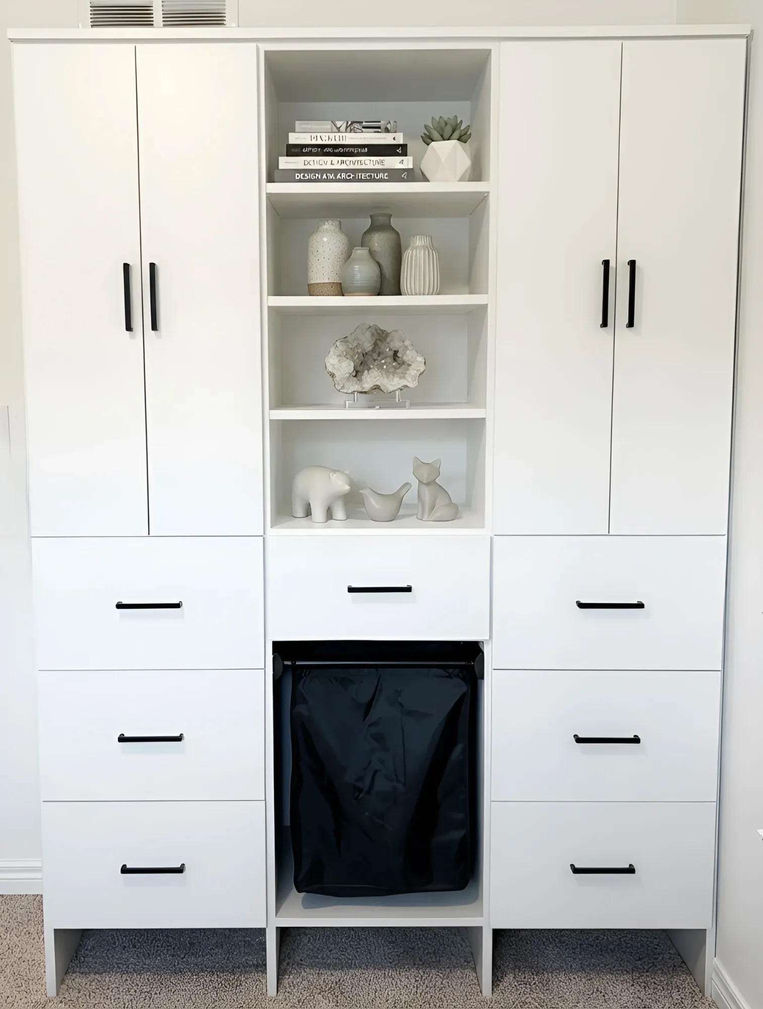 A white wardrobe with two full-height cupboards either side of open display shelving, six drawers, and a pull-out laundry hamper in the centre bay