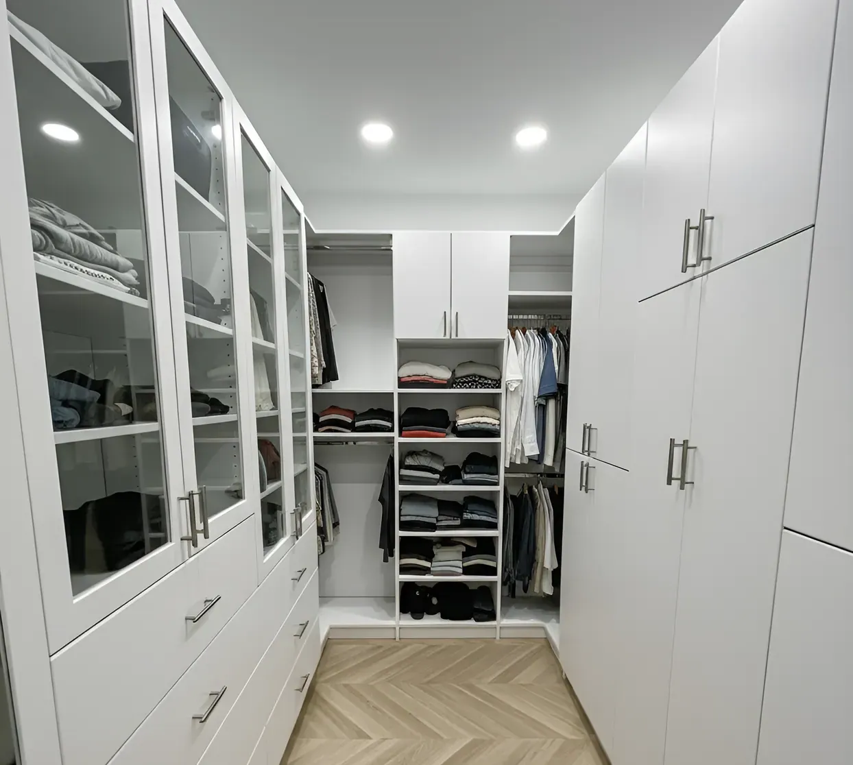 A custom walk-in closet built by Closet Form, glass-fronted cabinets down one side and hanging over folded shelving at the end
