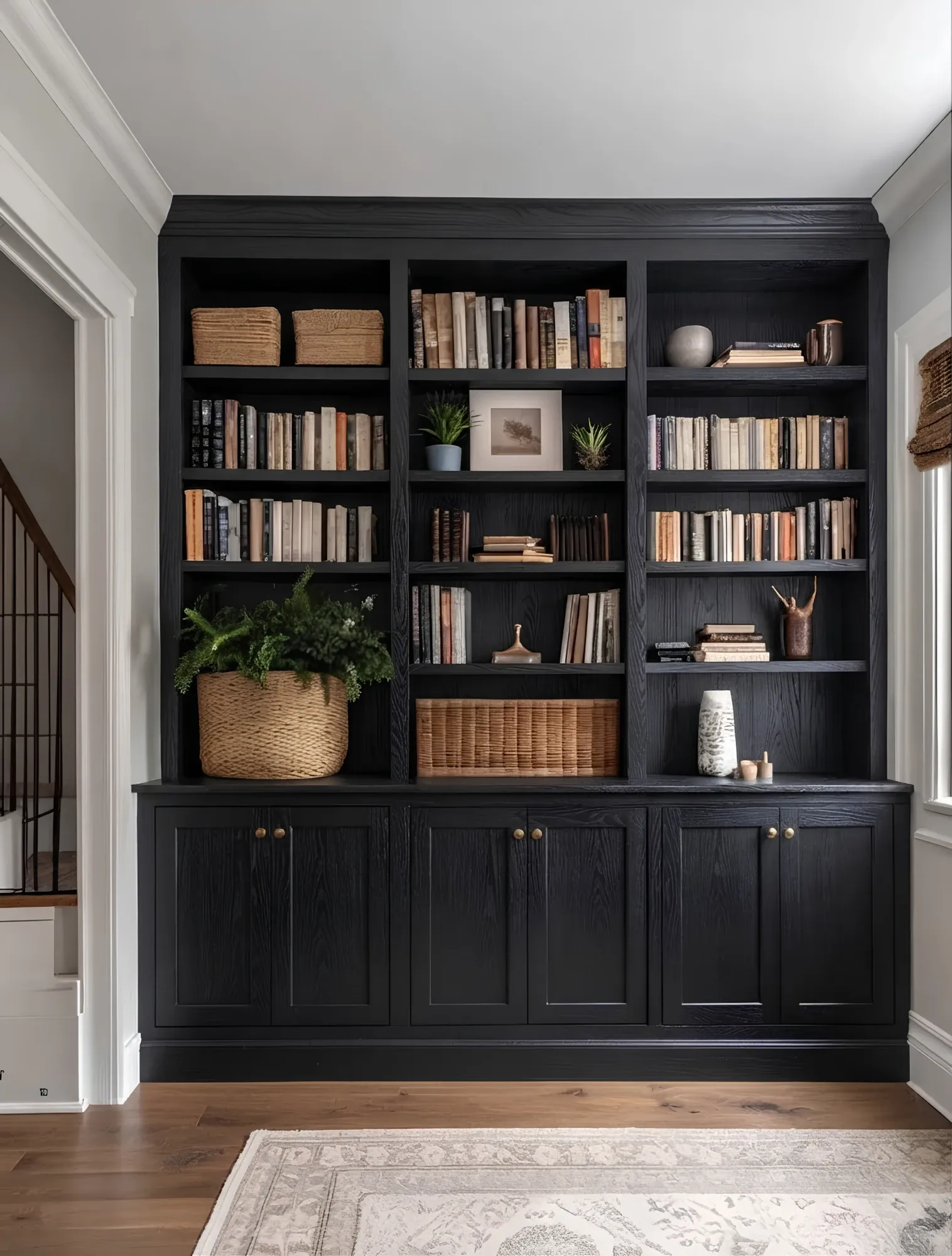 A black oak bookcase wall, three bays of open shelving carried to the crown over a run of cupboards