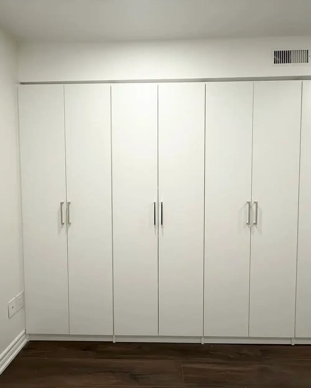 A run of floor-to-ceiling white built-in wardrobes with flat slab doors, fitted wall to wall in a Toronto bedroom