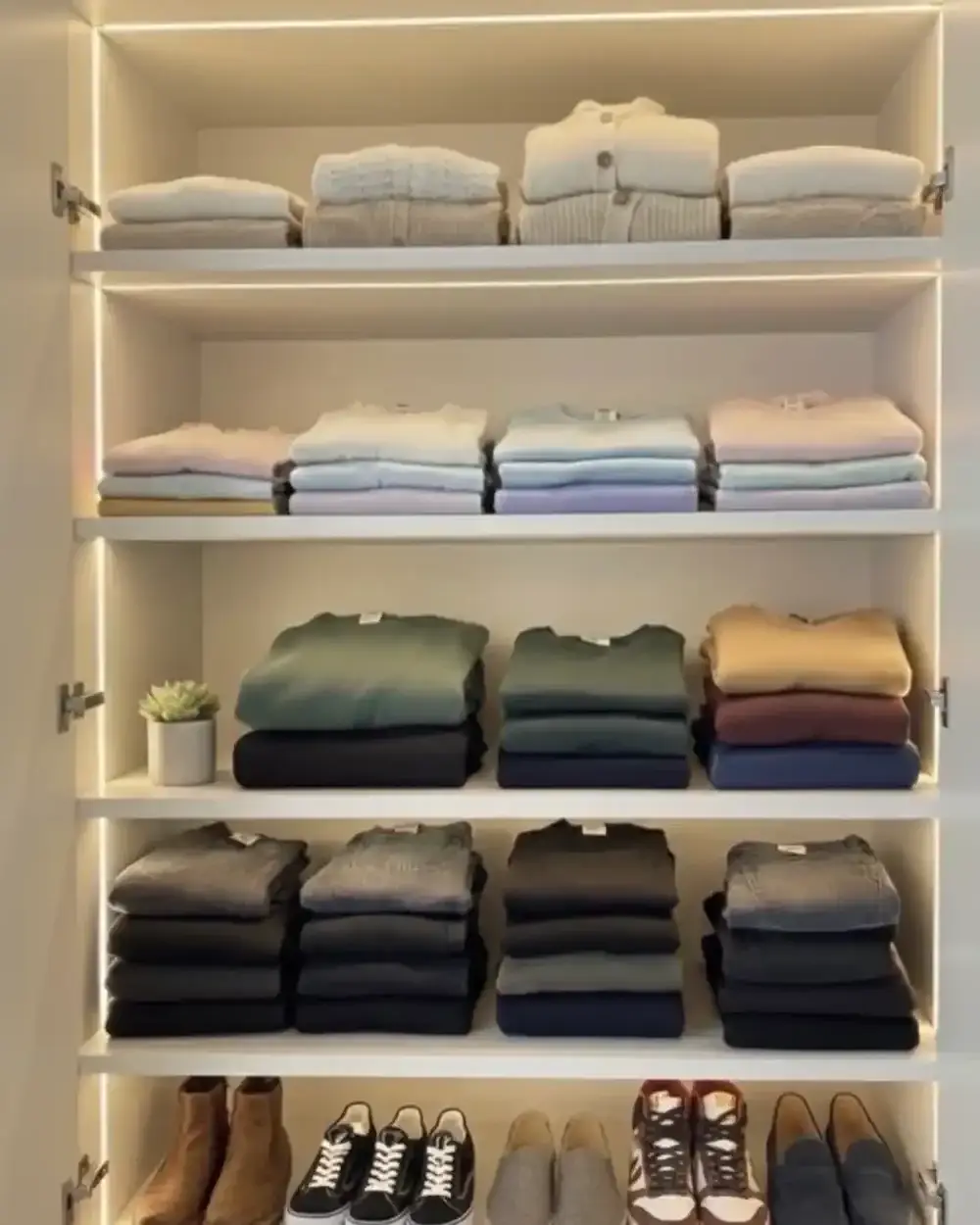 Warm LED strips under each shelf of a closet, lighting stacks of folded knitwear from above