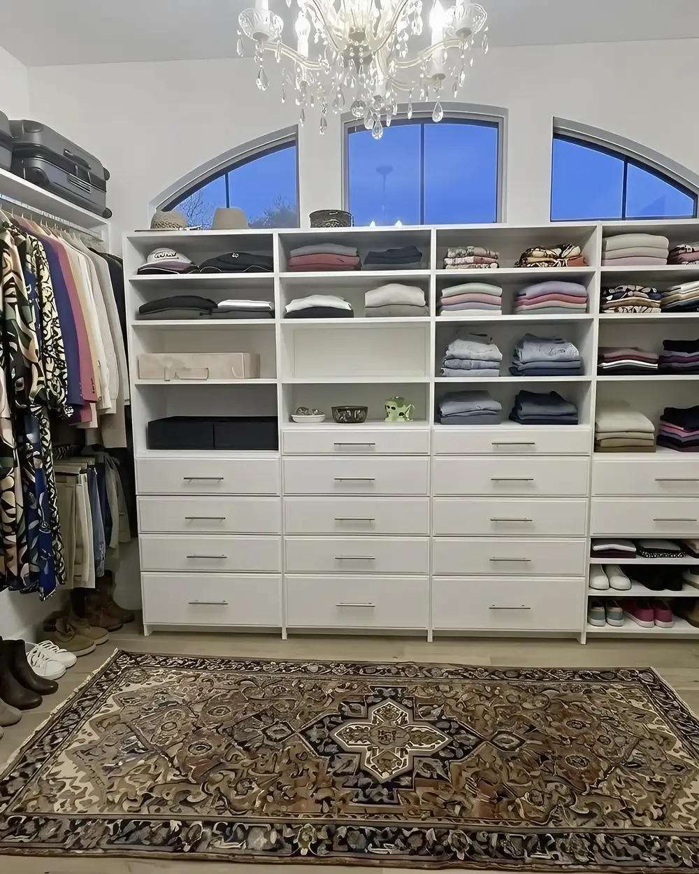 A white custom closet built under an arched window, with drawer banks and a patterned rug on the floor