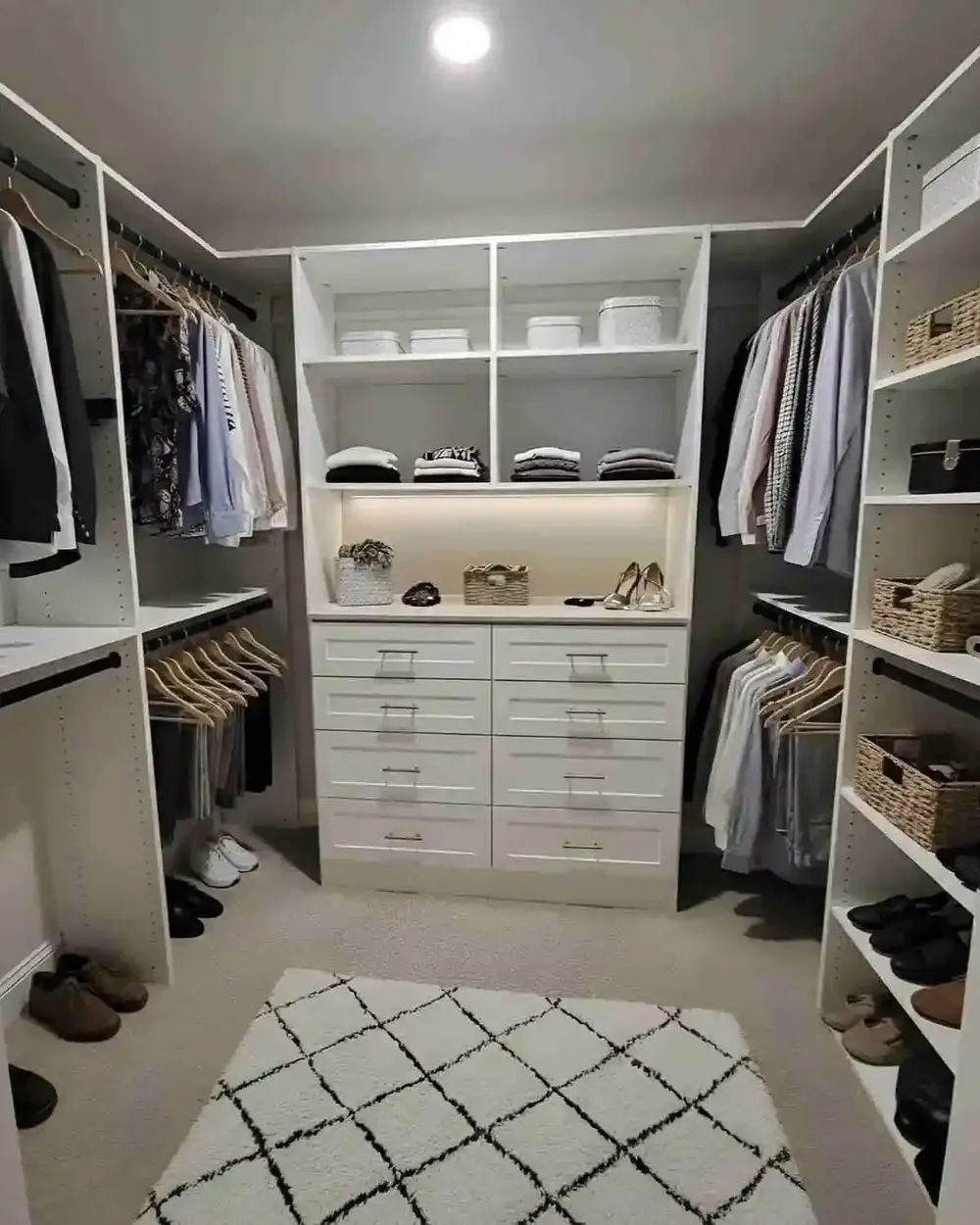 A walk-in closet with a lit display shelf, drawer banks, shoe shelving and a patterned rug
