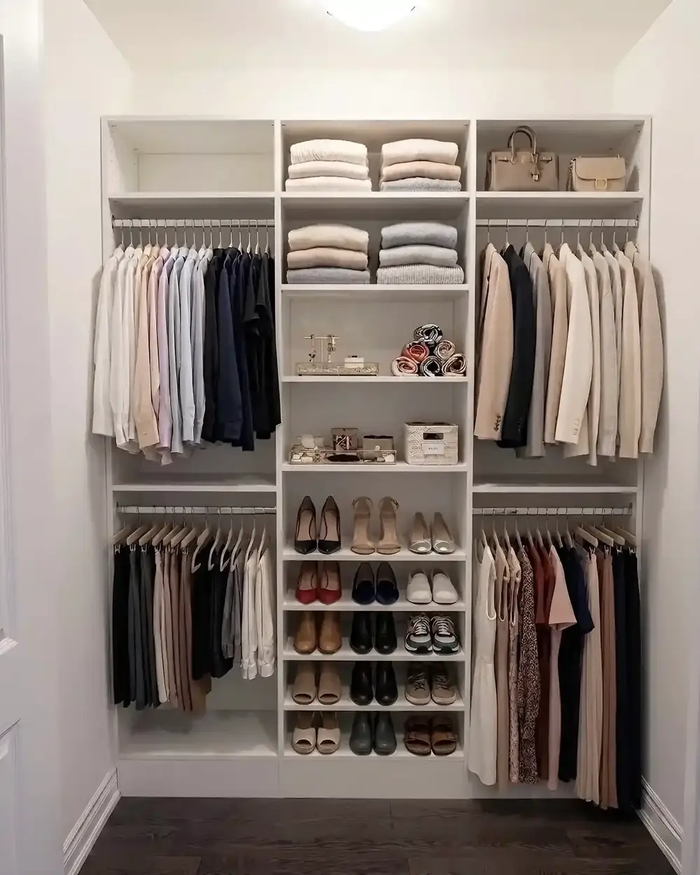 A white reach-in closet with folded linens on the top shelf, hanging below and shoe shelves to one side