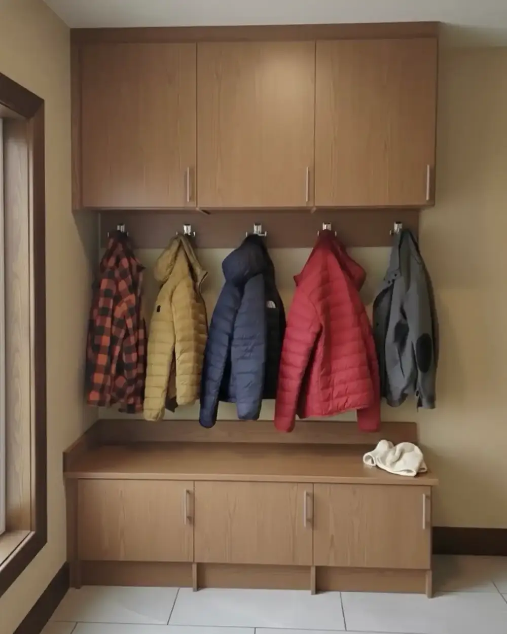 A light oak entryway bench with coats hanging from hooks on the panelled wall above